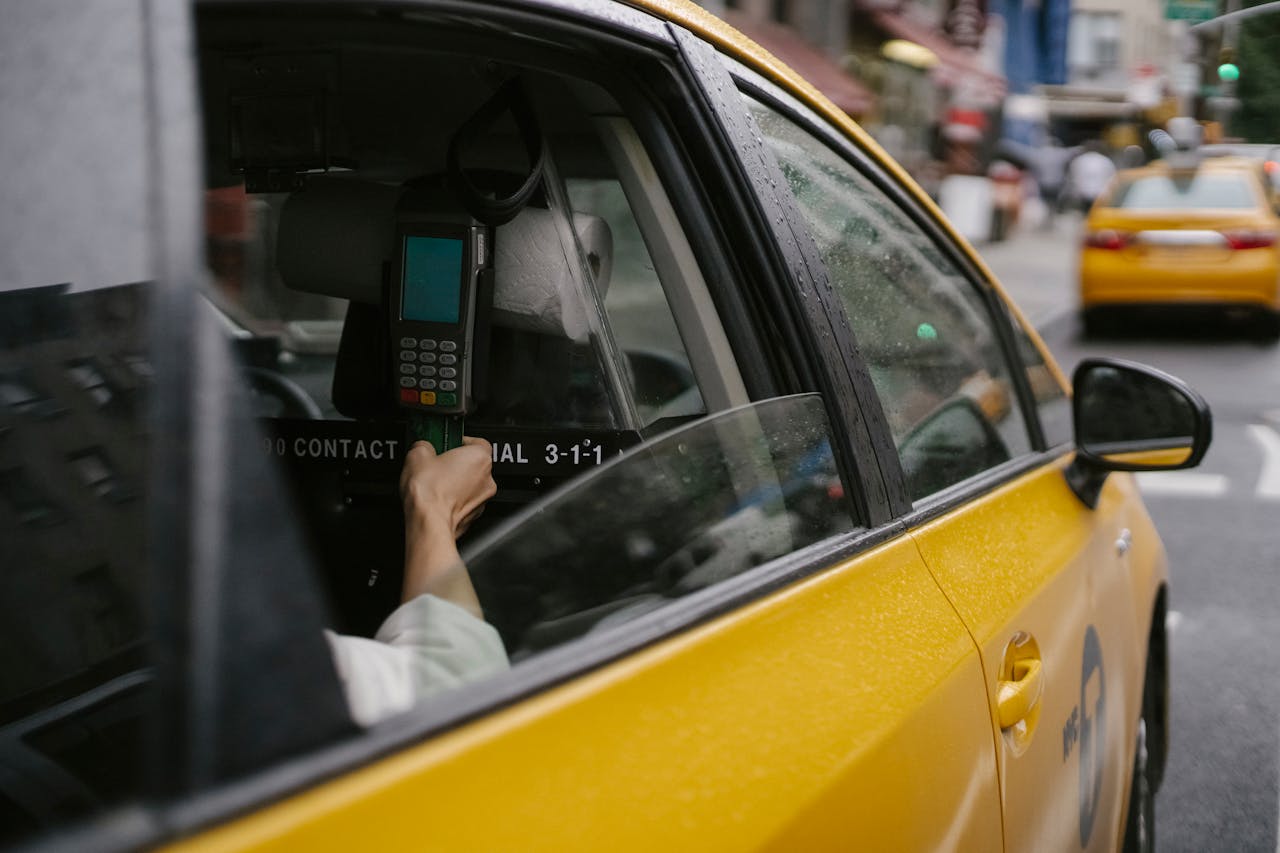Close-up of passenger's hand using payment terminal inside a yellow taxi cab on a city street.