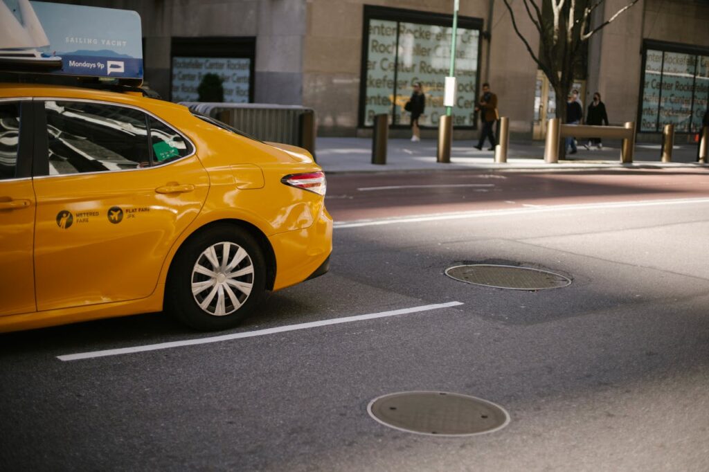 Modern bright cab driving near sidewalk and modern buildings on asphalt road on urban background in town in soft daylight